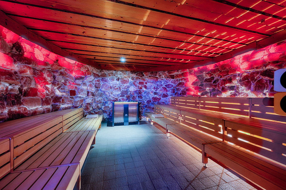 Sauna im Welcome Hotel Bad Arolsen mit Holzbänken, Natursteinwänden, Holzdecke und stimmungsvoller rot-blauer Beleuchtung.