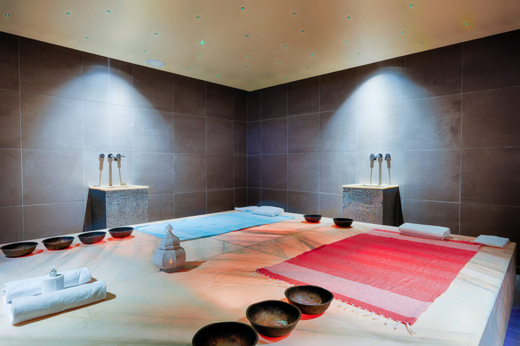 Hamam im Welcome Hotel Bad Arolsen mit beheizter Marmorliege, farbigen Liegetüchern, Wasserschalen und gedämpfter Beleuchtung im Wellnessbereich.